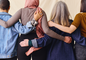 A group of four women supporting each other by standing and holding their back, showcasing unity, friendship, and the power of female connection on International Women's Day.